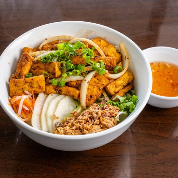 Vietnamese tofu vermicelli bowl with vegetables, fried onions, and a side of sauce.
