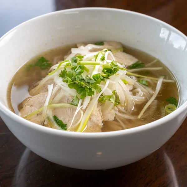 A white bowl of Pho Town's Vietnamese pho with chicken, noodles, broth, onions, and cilantro.