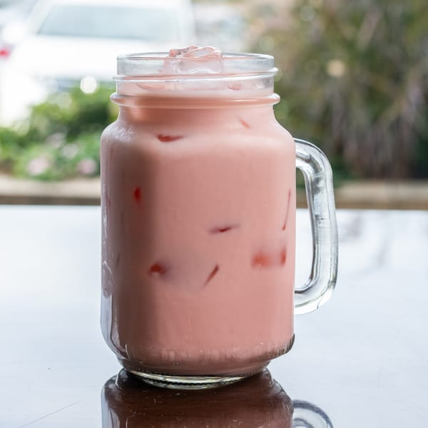 Pink Vietnamese iced drink with ice cubes in a glass mason jar on a reflective table.