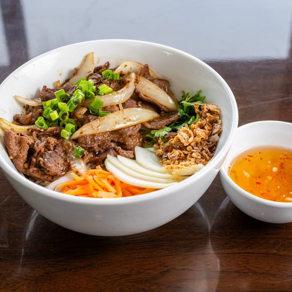 Vietnamese beef and onion stir-fry with scallions, fried garlic, pickled carrots, and daikon, served with sauce.