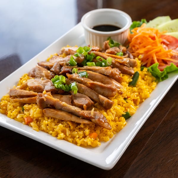 Vietnamese grilled pork over yellow fried rice, garnished with green onions, and a side salad.