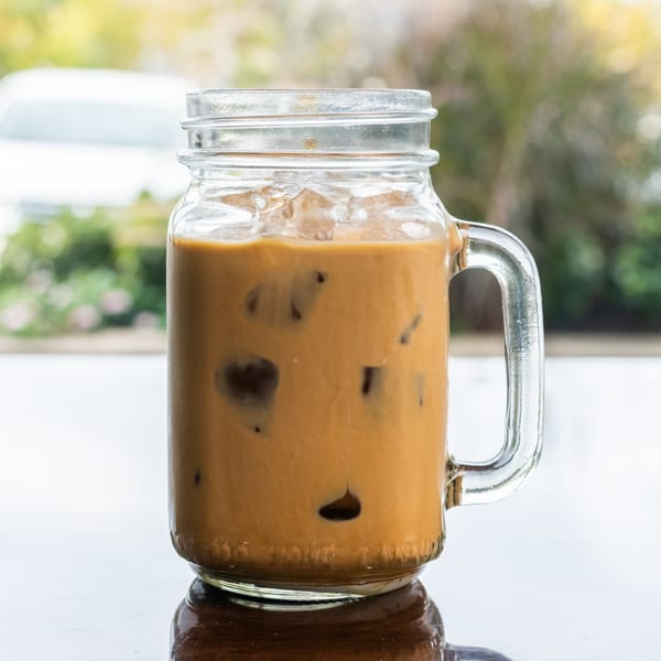 Iced Vietnamese coffee in a mason jar mug with ice, on a reflective surface.