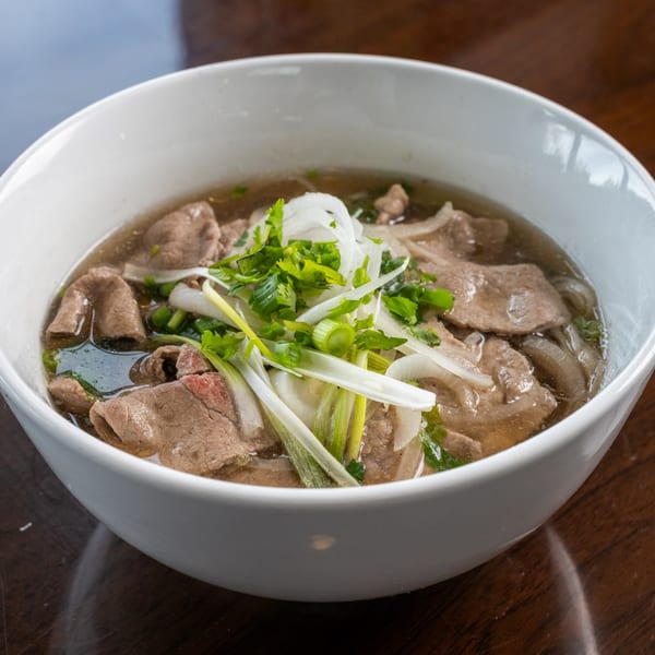 Close-up of a bowl of Pho Town's Vietnamese pho with beef, noodles, onions, and herbs.