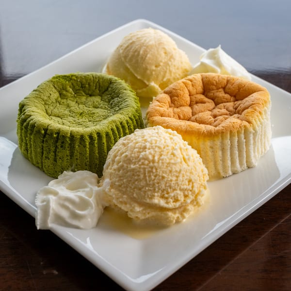 Two Japanese cheesecakes, one matcha and one original, with scoops of vanilla ice cream and whipped cream.