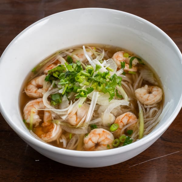 A white bowl of Pho Town's shrimp pho, garnished with fresh herbs and sliced onions.